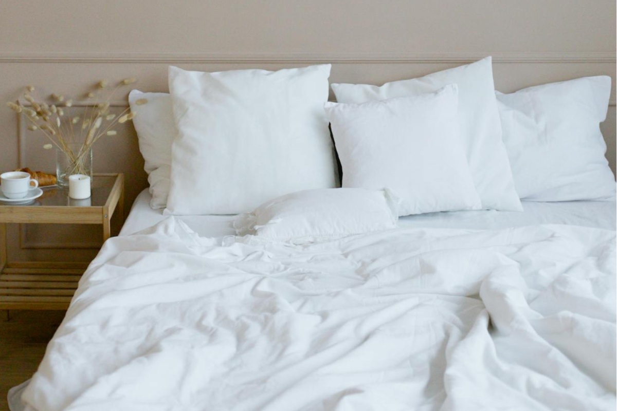 A bed made with cooling sheets for hot sleepers, featuring a light duvet and minimalist decor, conveying a fresh and airy feel.