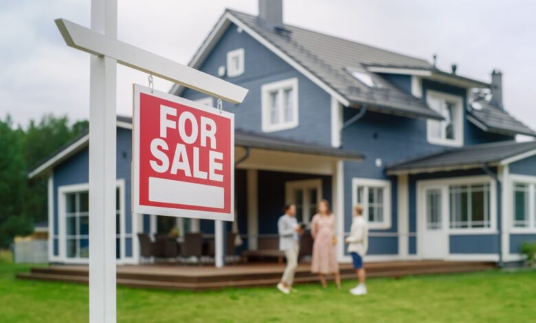 A couple talking to their realtor behind a "for sale" sign after the home inspection