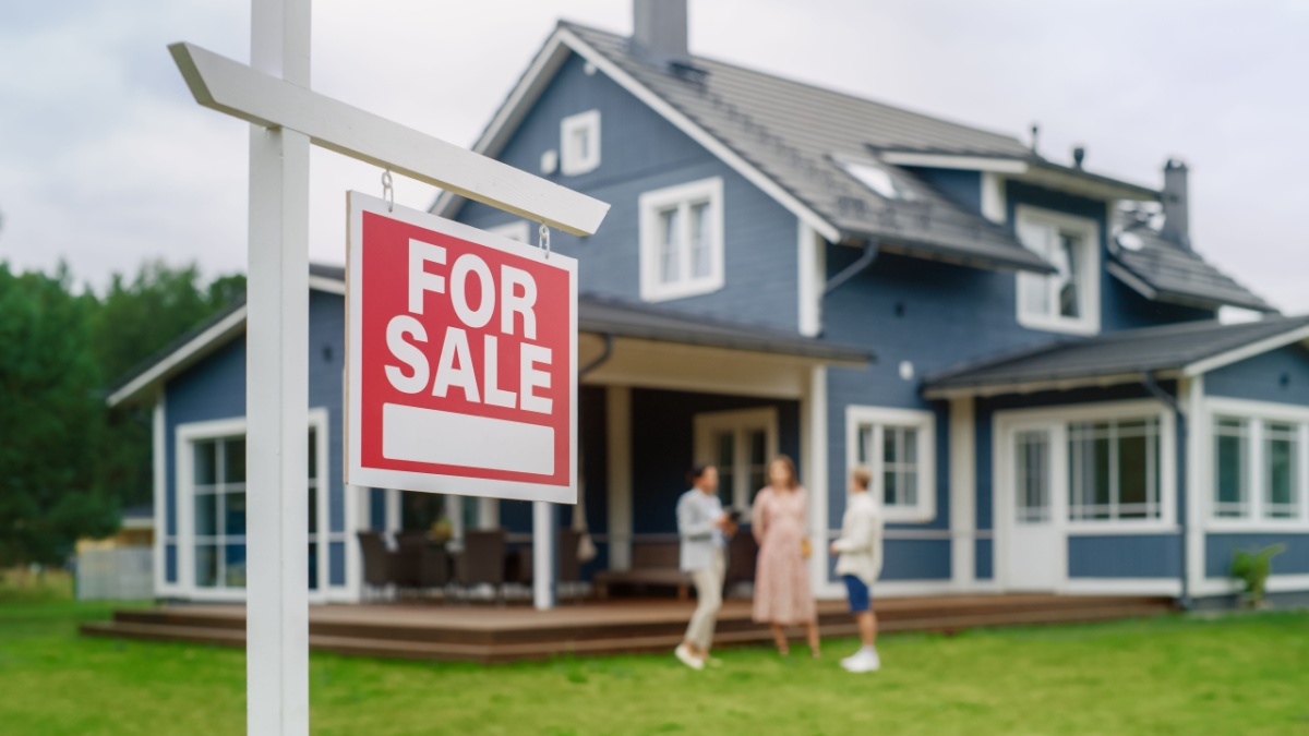A couple talking to their realtor behind a "for sale" sign after the home inspection