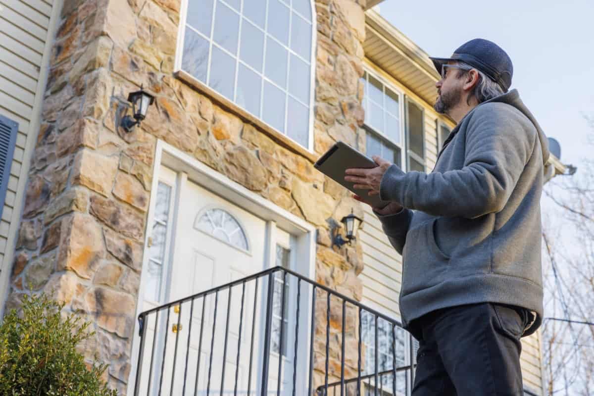 home appraiser standing outside a home looking up at exterior window