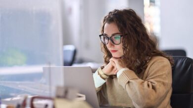 A young woman sits in front of a laptop looking at tips about how to us AI to search for a home with Redfin.